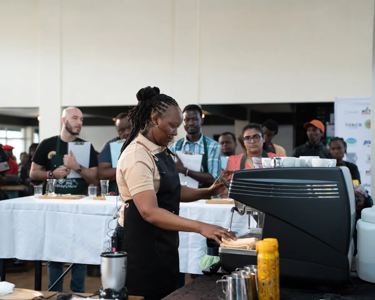 The finalist working the espresso machine with judges behind her