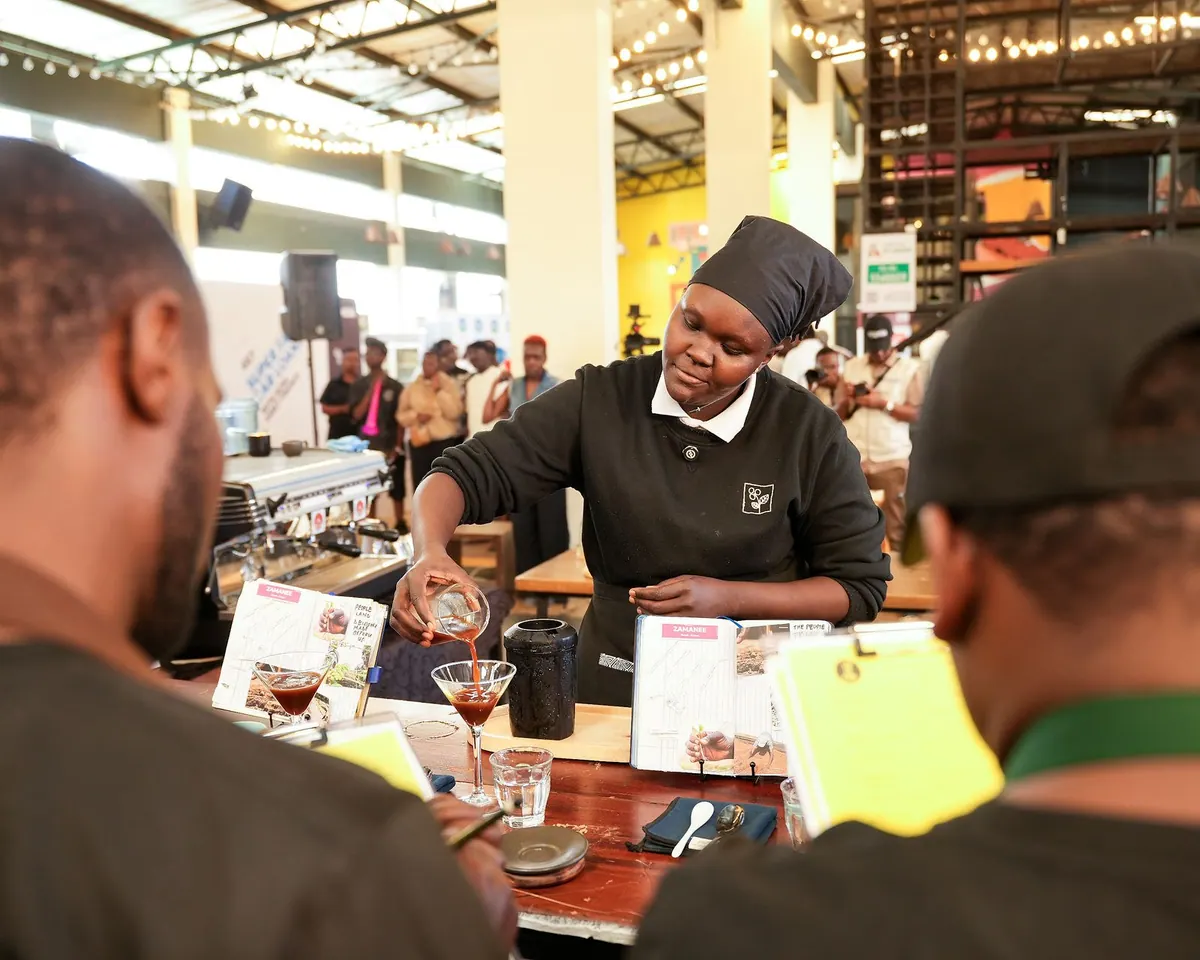 A barista pouring into stemmed glasses in front of the judges