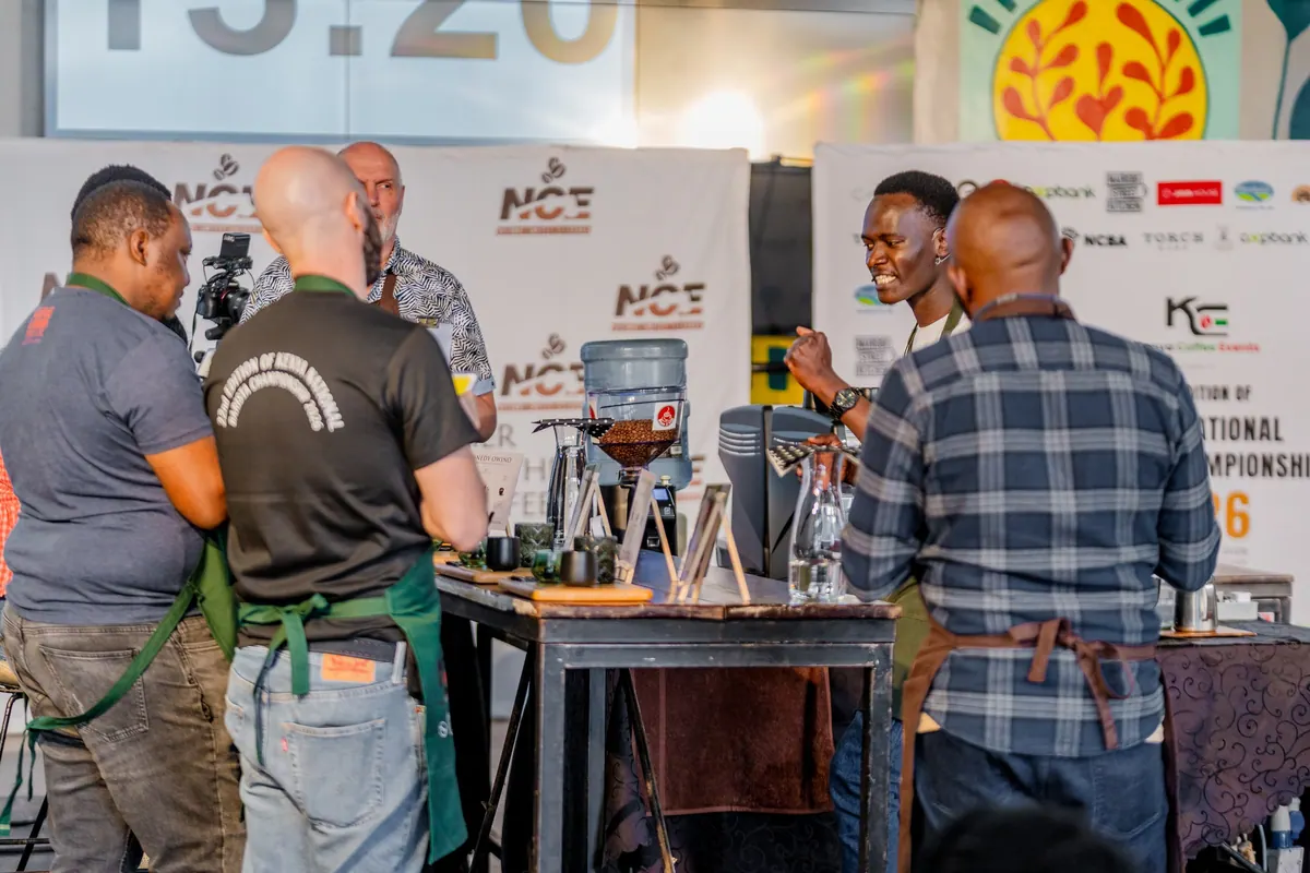 Competitors and judges around a brewing station under the event clock